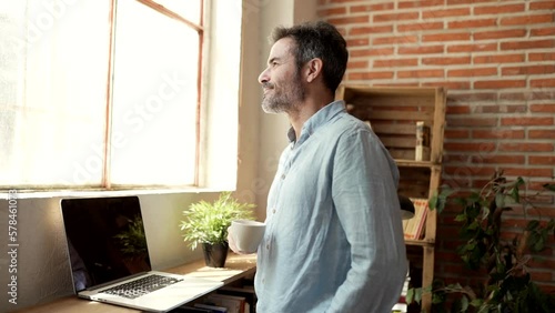 mature man at home looks out the window while having a glass of coffee for breakfast photo