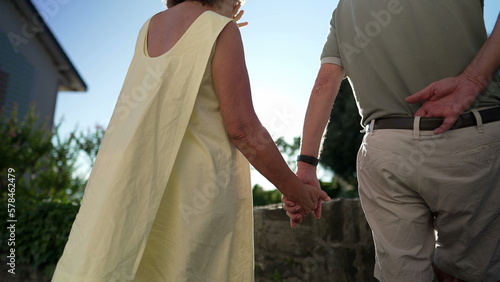 Senior married couple hands held together standing outdoors with sun flare. Close up of older people in love and support