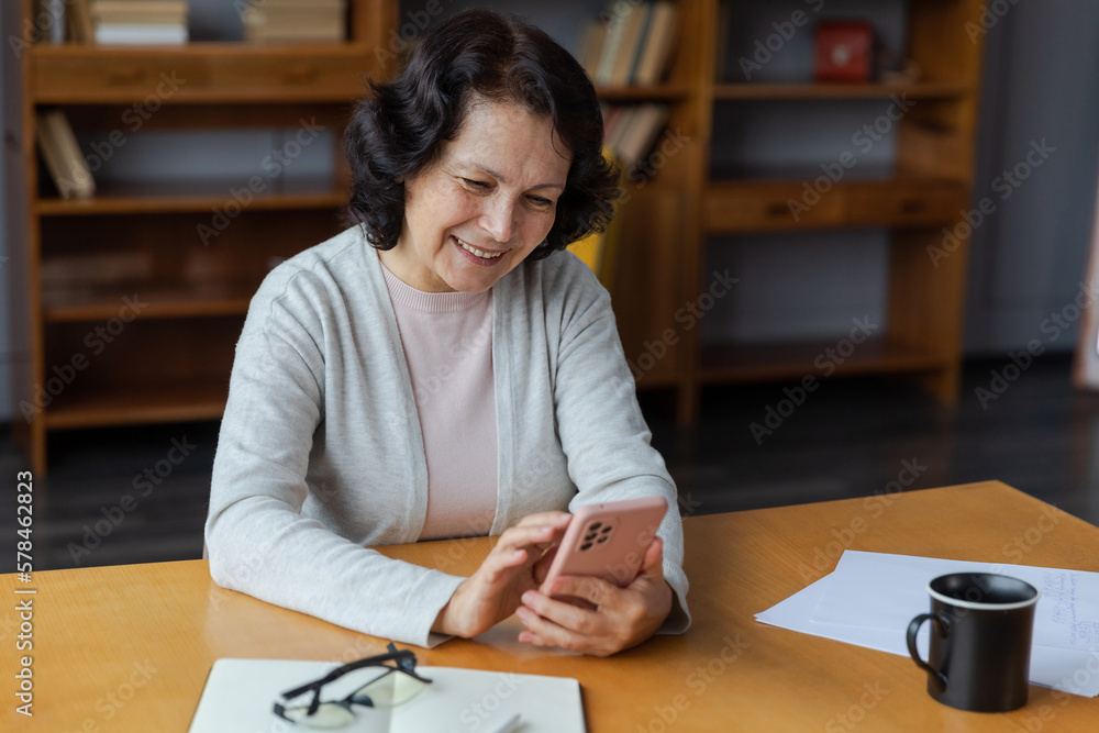 European middle aged senior woman holding using smartphone touch screen typing scroll page. Stylish older mature 60s lady with cell phone using internet social media apps at home. Shopping online. European middle aged senior woman holding using smartphone touch screen typing scroll page. Stylish older mature 60s lady with cell phone using internet social media apps at home. Shopping online.