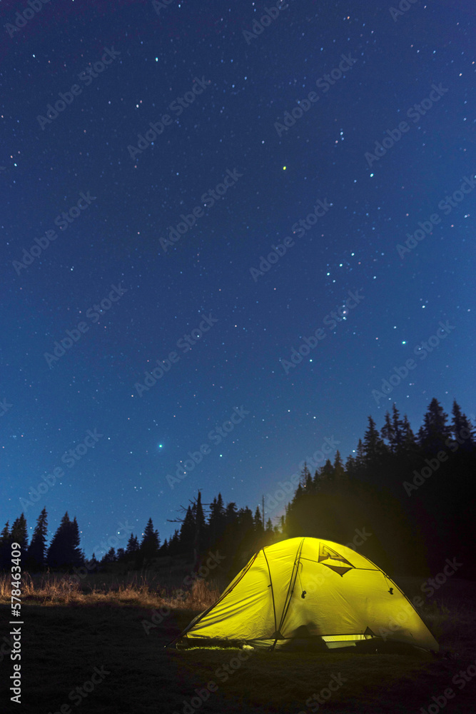 Luminous tourist tent under the starry sky. Tourist tent at night in the forest. Starry sky above the tent.