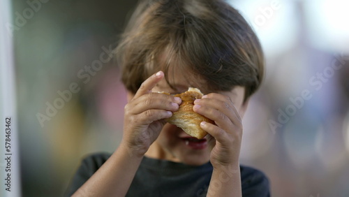Portrait of child eating piece of bread croissant. Close up face of one small boy kid eating carb food