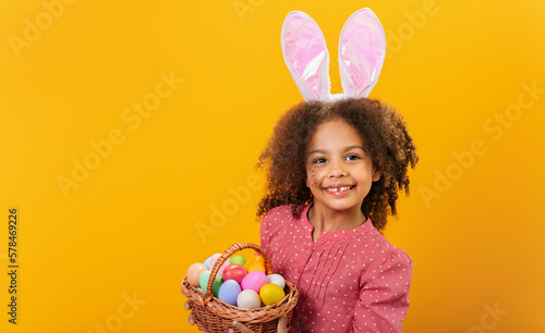 Fotografia A Black girl with rabbit ears on her head with a basket full of colored eggs