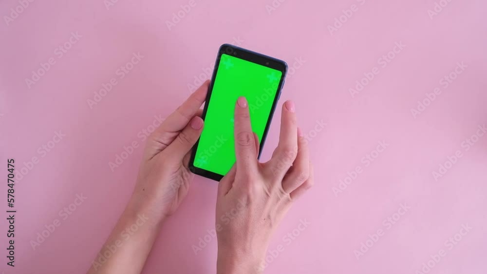 Close-up of female hands scroll phone with green screen on pink background Close-up of female hands scroll phone with green screen on pink background