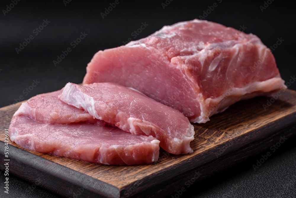 Fresh juicy pork on a wooden cutting board with spices and salt