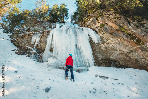 Photography Ice climber dressed warm winter climbing clothes, safety harness and helmet under the frozen waterfall