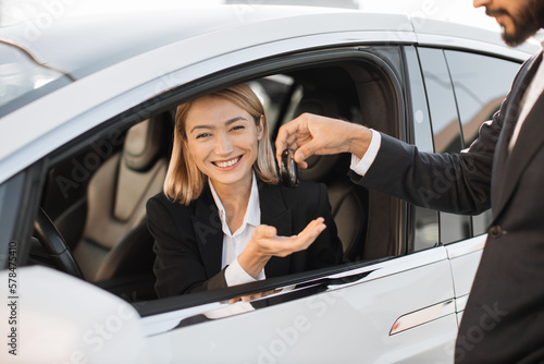Charming caucasian woman in formal wear siding inside her luxury new car and receiving keys from male dealer. Successful business lady making expensive purchase. © sofiko14