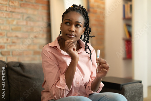 Hesitant black woman thinking what better to choose during critical days, holding menstrual tampon and thinking