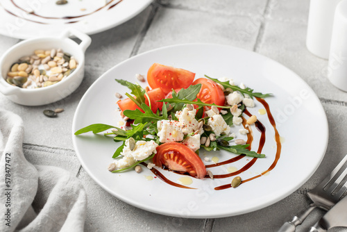 Healthy vegetable salad with fresh arugula, tomato, feta cheese on white plate with cutlery, gray tile background. Diet menu. Appetizer salad