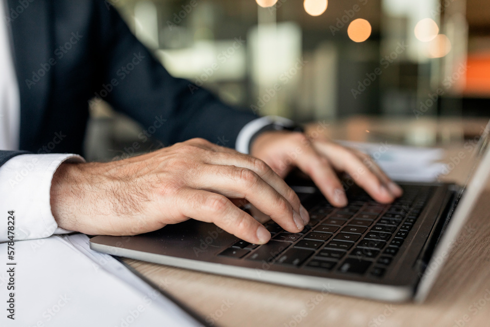Closeup businessman using laptop, typing on keyboard, writing email, sitting at desk in office, selective focus Closeup businessman using laptop, typing on keyboard, writing email, sitting at desk in office, selective focus