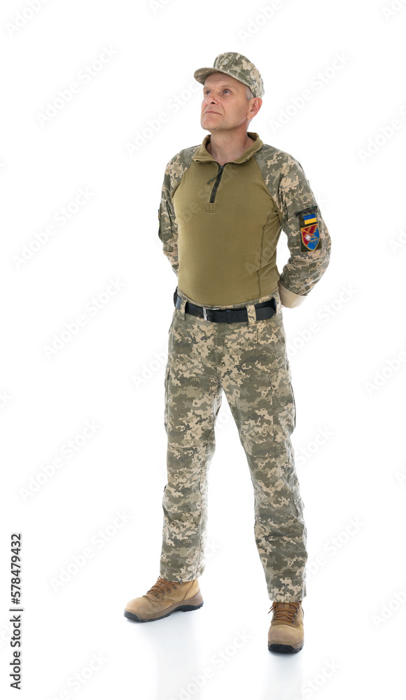 Ukraine army soldier put his hands behind his back isolated on white background. Full length portrait of old defender seriously looking into the distance and posing in studio. Stand for Ukraine. Ukraine army soldier put his hands behind his back isolated on white background. Full length portrait of old defender seriously looking into the distance and posing in studio. Stand for Ukraine.