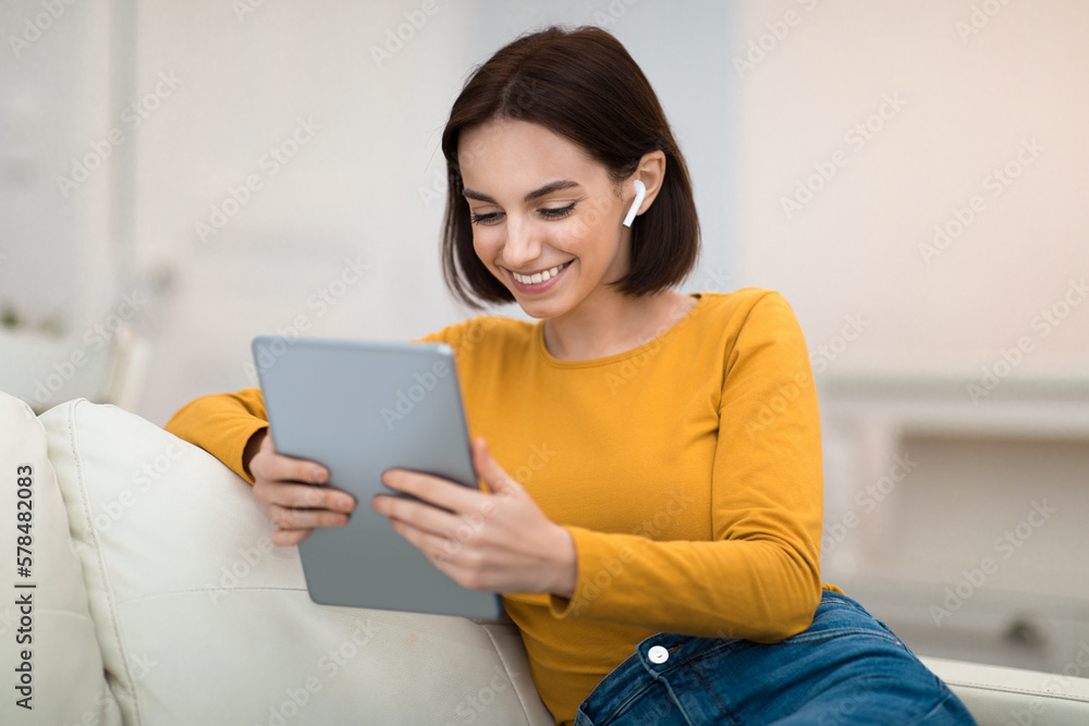 Cheerful beautiful lady using digital pad and earpods at home Cheerful beautiful lady using digital pad and earpods at home