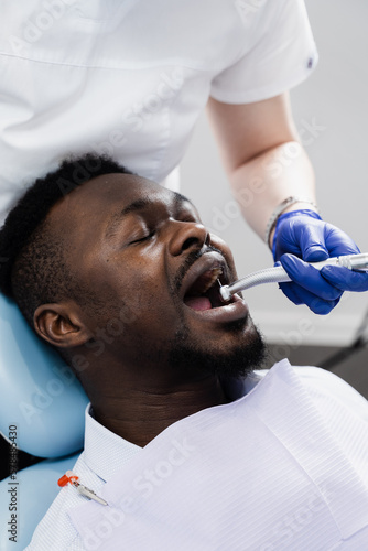 Dental drill for african man in dentistry clinic. Dentist is removing caries and filling teeth for african american patient.