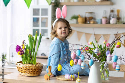 Photography Portrait of cute pretty smiling little girl in blue dress and bunny rabbit ears preparing easter table decor