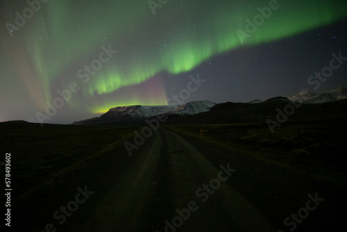 Red and green aurora borealis over mountain road, Iceland