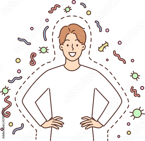 Happy man with good immunity smiling and holding hands on belt standing among bacteria and parasites