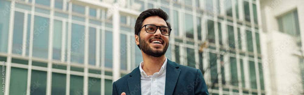 Smiling indian businessman in suit and glasses with laptop near office building Smiling indian businessman in suit and glasses with laptop near office building