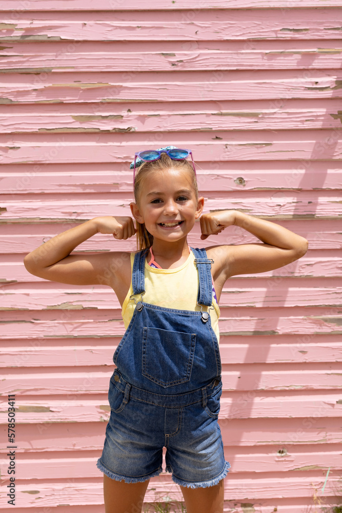 Portrait of happy biracial girl smiling and showing muscles over pink wall - obrazy, fototapety, plakaty 
