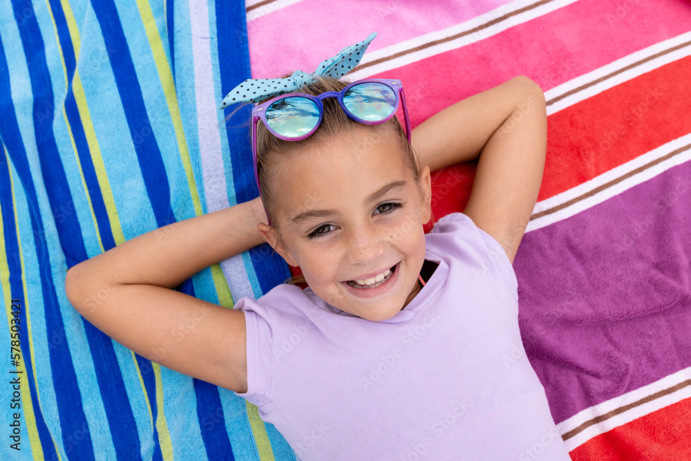 Portrait of happy biracial girl smiling and lying on towel by the swimming pool - obrazy, fototapety, plakaty 