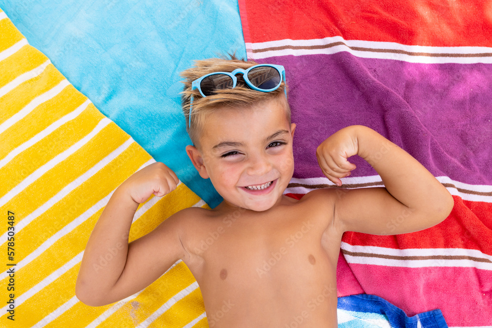 Portrait of happy biracial boy smiling and lying on towel by the swimming pool - obrazy, fototapety, plakaty 