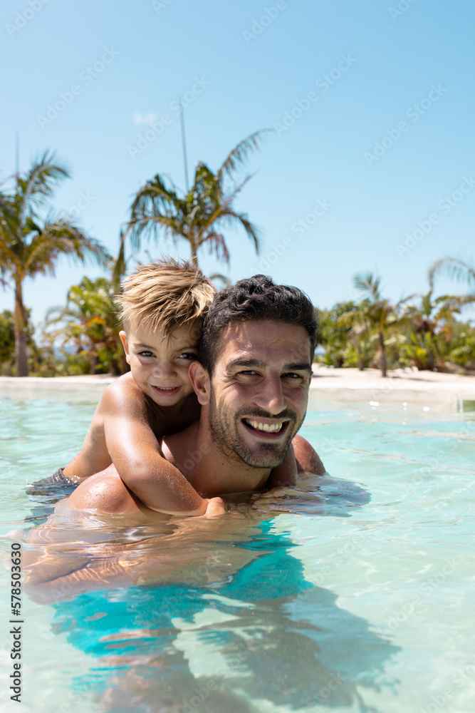 Fototapeta premium Portrait of happy biracial father and son playing together in swimming pool