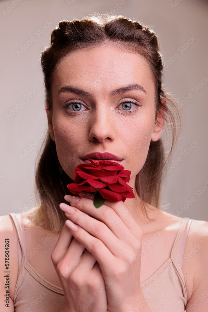 Beautiful fashion model holding red flower near lips portrait. Attractive young caucasian woman kissing rose petals, showing love and tenderness emotions looking at camera Beautiful fashion model holding red flower near lips portrait. Attractive young caucasian woman kissing rose petals, showing love and tenderness emotions looking at camera