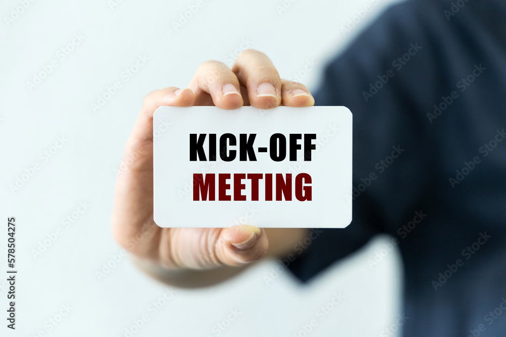 Kick off meeting text on blank business card being held by a woman's hand with blurred background. Business concept about kick off meeting. Kick off meeting text on blank business card being held by a woman's hand with blurred background. Business concept about kick off meeting.