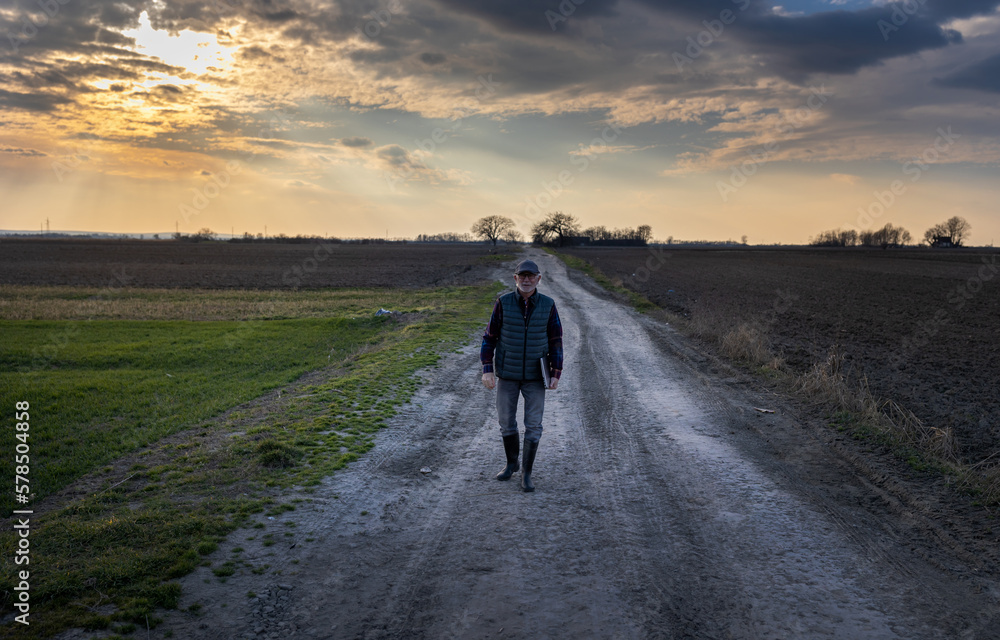 Obraz premium Senior farmer walking on dirty road