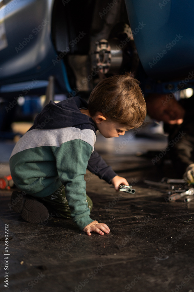 Little boy helps his dad in the garage to repair the car. Time with father.