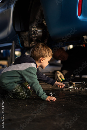 Little boy helps his dad in the garage to repair the car. Time with father.