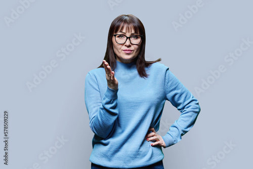 Serious middle aged woman gesturing looking in camera on gray background