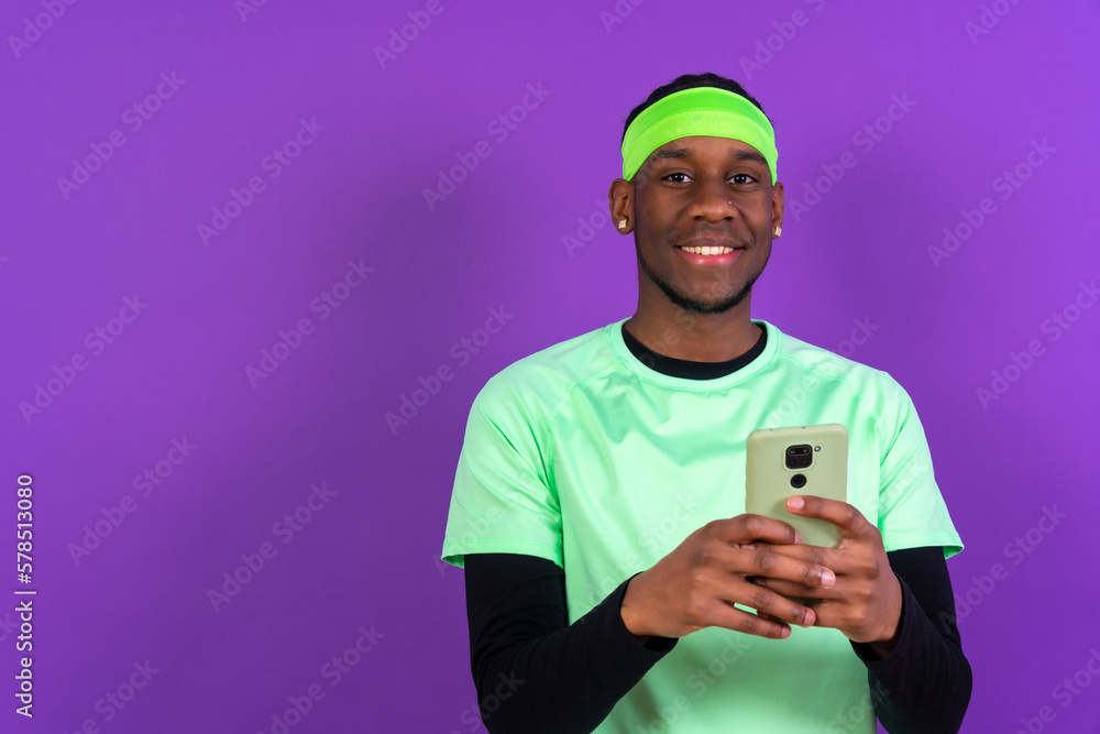 Black ethnic man with a phone in green clothes isolated on purple background Black ethnic man with a phone in green clothes isolated on purple background