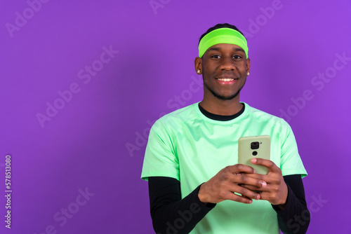 Black ethnic man with a phone in green clothes isolated on purple background © unai