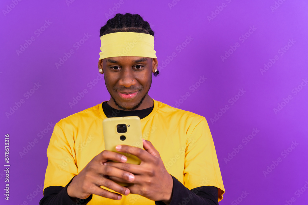 Black ethnic man with a phone in yellow clothes on a purple background, smiling Black ethnic man with a phone in yellow clothes on a purple background, smiling