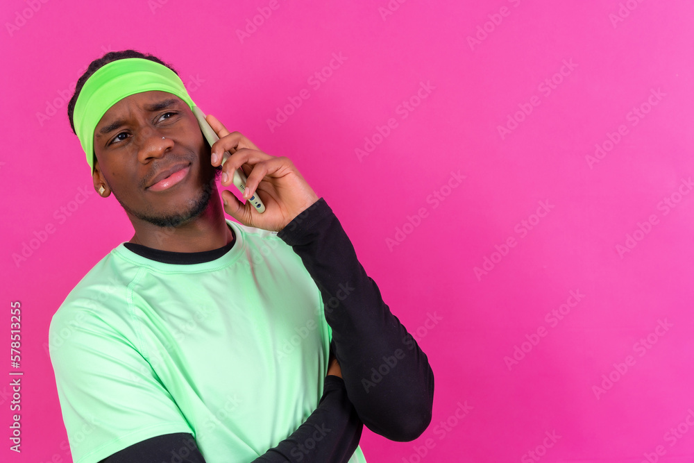 Black ethnic man with a phone in green clothes on a pink background, serious talking on the phone Black ethnic man with a phone in green clothes on a pink background, serious talking on the phone