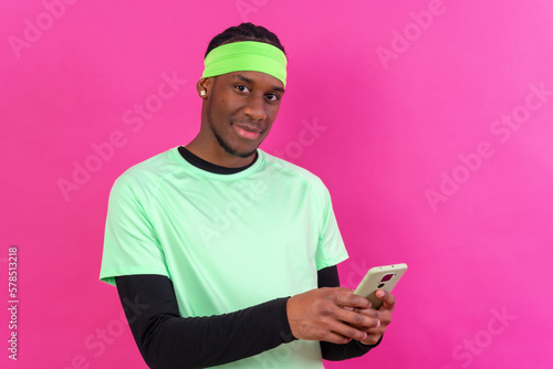 Black ethnic man with a phone in green clothes on a pink background, smiling © unai