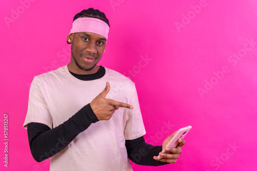 Black ethnic man with a phone in pink clothes on a pink background, talking on the phone