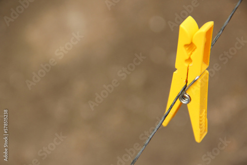 A yellow plastic clothes pin hanging on a wire photo