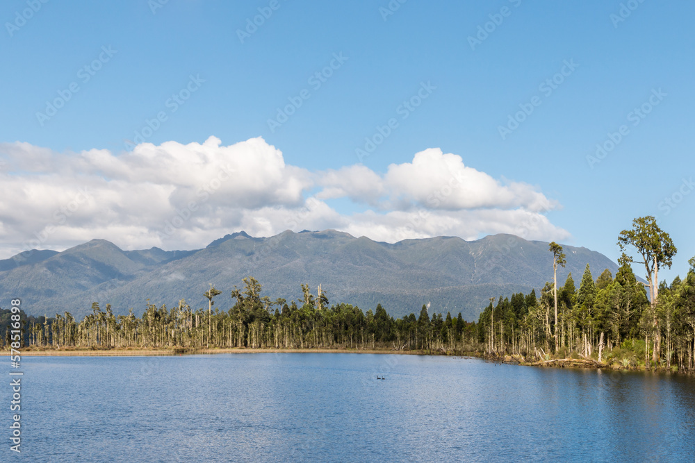 Lake Brunner on the West Coast of New Zealand South Island with Hohonu mountain range, podocarp trees, blue sky and copy space