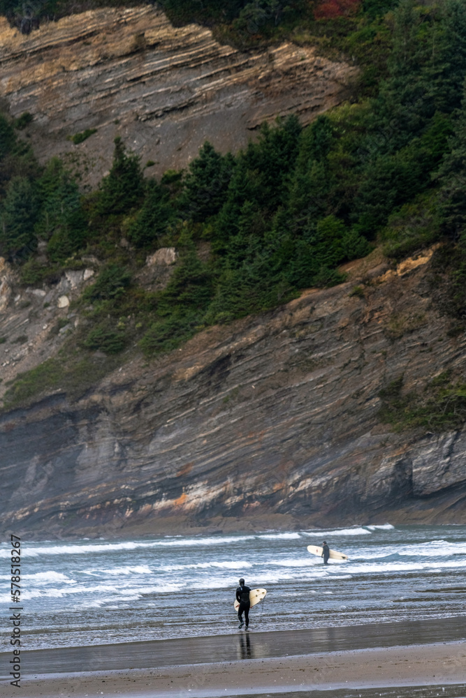 A couple of surfers enters the water with his board, at Oswald West State Park