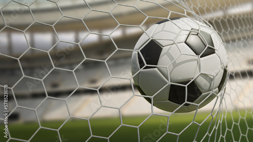 Football in goal net. Blurred footbal stadium in background during daytime.