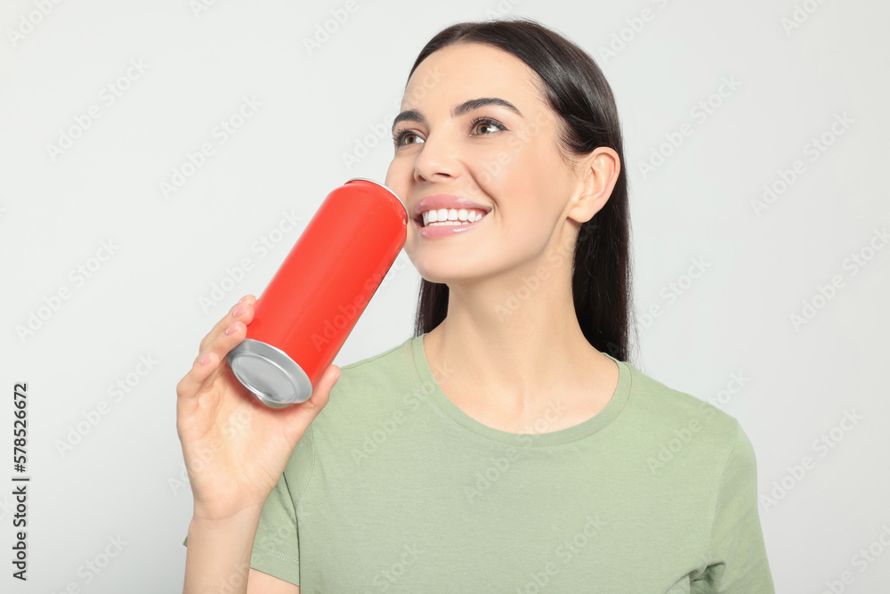 Beautiful happy woman holding red beverage can on light grey background Beautiful happy woman holding red beverage can on light grey background