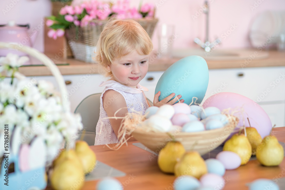 A little girl takes out a large painted Easter egg from a basket full of mcolorfu eggs. A child in a kitchen decorated for Easter after painting. A little girl takes out a large painted Easter egg from a basket full of mcolorfu eggs. A child in a kitchen decorated for Easter after painting.