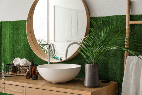 Vase with palm leaves  sink and cosmetic products on table in bathroom