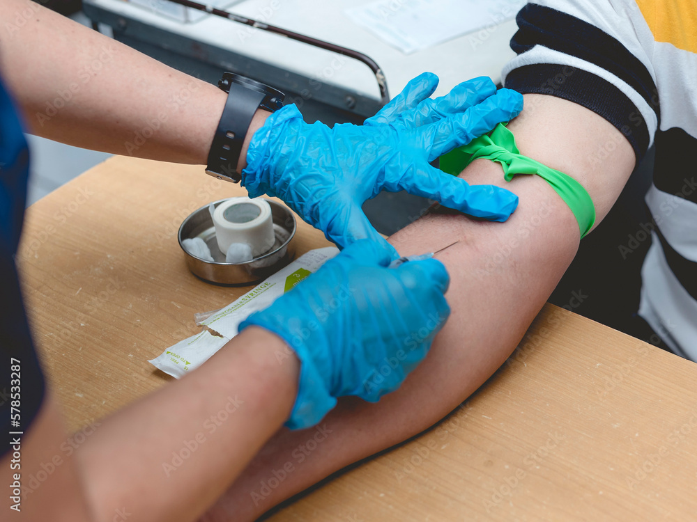 A nurse or phlebotomist draws blood from the vein of a patient. An IV