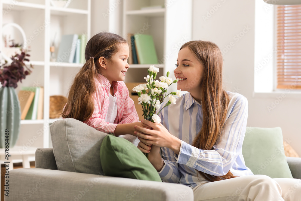 Cute little girl greeting her mother with flowers at home on holiday