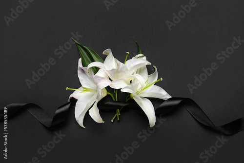 Black funeral ribbon and white lily flowers on dark background