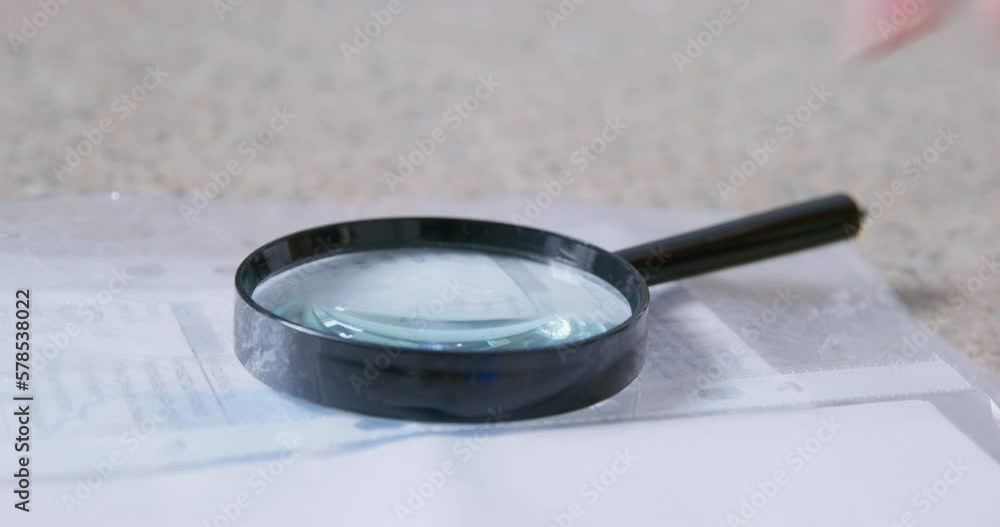 Hand of woman taking magnifier glass and putting back on pile of papers on blurred background. Reading glass on documents close view Hand of woman taking magnifier glass and putting back on pile of papers on blurred background. Reading glass on documents close view