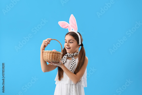 Little girl in bunny ears with basket of Easter eggs on blue background