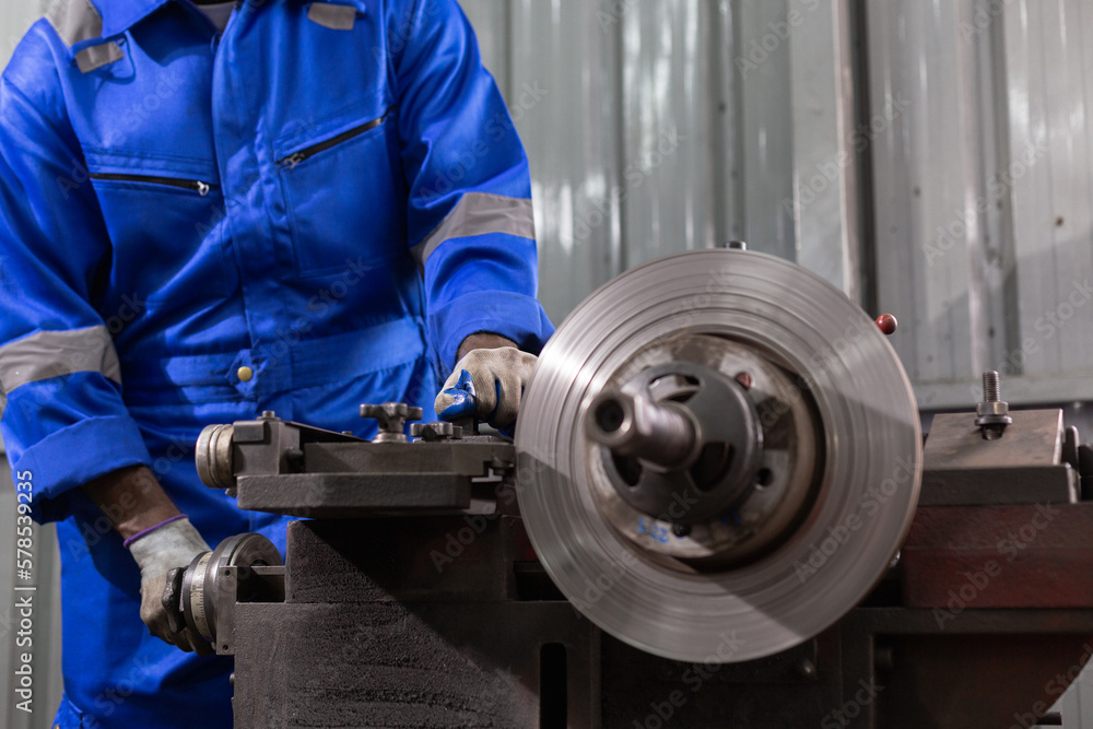 Engineering worker man wearing uniform safety working machine lathe metal brake disc grinder in factory industrial, worker manufacturing industry concept.