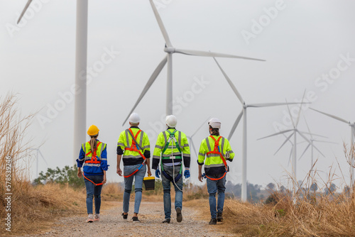Back view, Teamwork engineer worker wearing safety uniform discuss operational planning at wind turbine field renewable energy. technology protect environment reduce global warming problems.